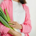 A woman in a pink jacket holding fresh spring onions against a white background.
